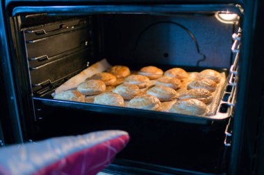 Human hand with an oven glove taking out of the oven a tray with pastry dumplings. Spain