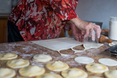 Unrecognizable aged woman cutting puff pastry with a glass to prepare dumplings. Spain