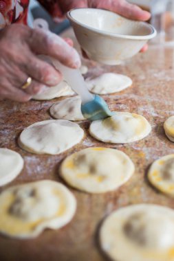 Close up of human hand preparing puff pastry damplings. Coating with whole egg pulp