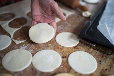 Unrecognizable aged woman holding puff pastry in circle with a glass. Preparing  dumplings