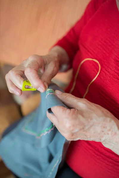 Unrecognizable senior woman doing embroidery with a yellow thimble. Interior