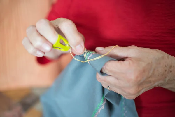 Senior woman sewing embroidery at home. Unrecognizable