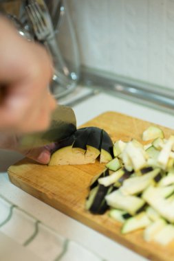 Ahşap bir masada patlıcan kesen beyaz bir adam. İç mekan