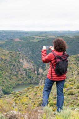 Dağlarda yürüyüş yapan bir kadın. Cep telefonuyla fotoğraf çekiyor.