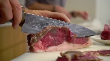 Hands of man cutting beef meat to make medium rare stakes on blurred background. Chef cooks delicious dinner with wife in kitchen closeup