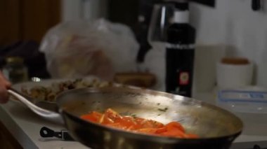 Housewife shakes pan to stir fresh cut tomatoes in hot oil. Woman cooks organic vegetables to serve with fried seafood for dinner closeup
