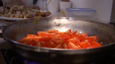 Sunflower oil poured on fresh cut tomatoes in silver pan on burning gas stove. Process of cooking vegetables to eat with seafood closeup