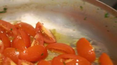 Housewife stirs fresh cut tomatoes in oil on hot pan. Process of preparing vegetables for organic dinner in kitchen at home closeup