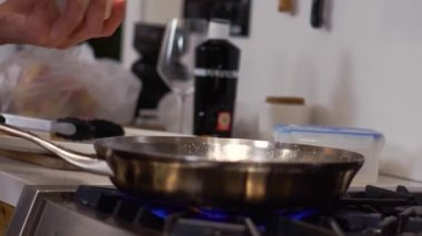Hand of man throwing salt on seafood frying in silver pan on kitchen gas stove. Chef enjoys cooking delicious dinner at home closeup