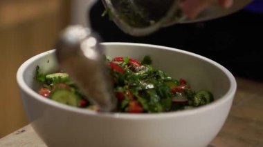 Housewife puts cooked organic salad into white bowl on blurred background. Dish with fresh vegetables ready to eat in kitchen closeup