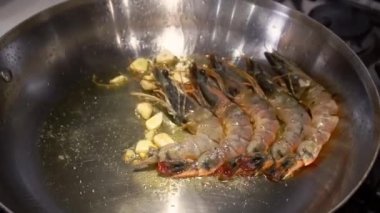 Raw shrimps frying with pieces of garlic on silver pan in kitchen. Process of preparing seafood for festive dinner at home closeup