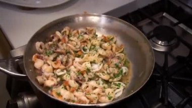 Housewife mixes seafood in oil shaking pan above burning stove in kitchen. Cooking process of delicious organic dish at home closeup