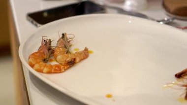 Woman puts fried shrimps on big white plate with utility tongs. Housewife serves seafood on tableware for evening dinner at home closeup