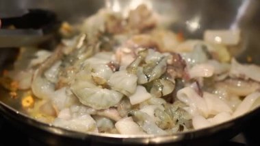 Housewife mixes raw seafood and garlic in pan with utility tongs. Woman prepares delicious vegan dinner in kitchen at home closeup