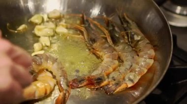 Hand of woman turning shrimps flying in oil with garlic on pan in kitchen. Housewife cooks delicious seafood for dinner at home closeup