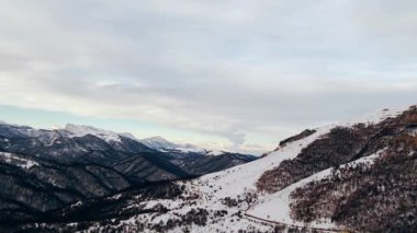 Giant Caucasus canyon with forestry hills and steep slopes under cloudy sky. Mountains covered with white snow on winter day aerial view