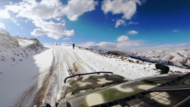 Karlı yolda araba sürerken, adam yol kenarında koşuyor. Mavi gökyüzünün altında, bulutlu bir şekilde. Kafkasya 'da kış gezisi araçtan görülüyor.