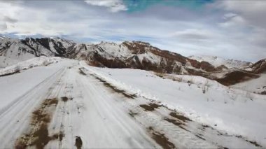 Bulutlu gökyüzünün altında, dağlık bölgede beyaz karlı yol dönüyor. Kış günü manzaralı muhteşem Kafkasya dağlarına arabayla maceralı bir yolculuk.