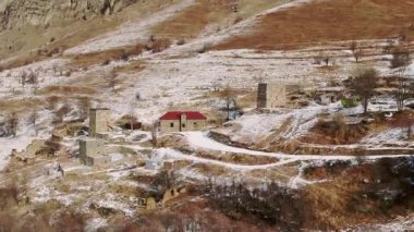 Kırmızı çatılı küçük bir ev ve kış günü karlı dağlık arazide binalar. Kafkasya dağlarının manzarası karla kaplı.