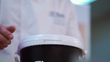 Aşçı plastik kovayı pasta malzemesiyle açar. Çörek yaymak için yeşillikli tuzlu sos. Fırında yemek pişirmek bulanık arka planda yakın plan