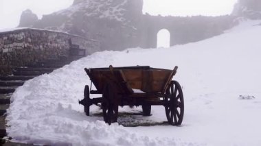 Tahta at arabası, taş merdivenlerin yanındaki karda duruyor. Sisli kış gününde Kafkasya dağlarında modası geçmiş dört tekerlekli taşımacılık