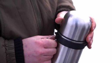 Adamın eli bulanık arka planda gümüş termosun kapağını çıkarıyor. Turist, Kafkasya dağlarında kış gezisinde çay içmek istiyor.