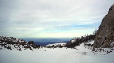 Dağlık arazide kayalar ve çıplak ağaçlarla kıvrımlı, karlı bir yolda araba sürüyor. Kafkasya 'daki maceralı kış gezisi araçtan görülüyor.