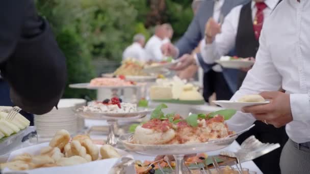 招待客はセルフサービスのテーブルで皿の上に食べ物をつかみ 豪華な結婚式をお楽しみください 人々は装飾が施されたオープン会場で結婚式を祝う — ストック動画