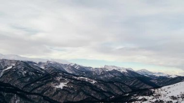 Giant Caucasus canyon with forestry hills and steep slopes under cloudy sky. Mountains covered with white snow on winter day aerial view