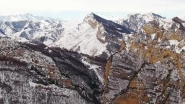Beyaz kar, bulutlu gökyüzünün altındaki Kafkas dağlarının dev kayalık tepelerinde uzanıyor. Soğuk kış havasında derin kanyonu olan devasa dağ sıraları.