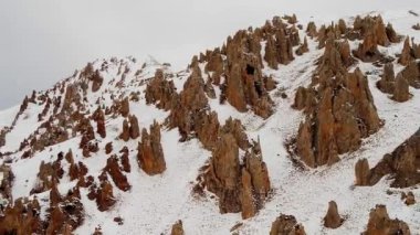 Rocks formed on slope of massive Caucasus mountain range canyon. White snow covers territory of highland on cloudy winter day aerial view