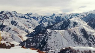 Rocky peaks around Caucasian mountain pass covered with white snow under cloudy sky. Scenic nature in highland on winter day aerial view