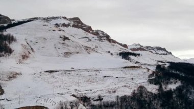 Arabalar, kış günü Kafkasya dağlarında dolambaçlı yollarda yol alırlar. Bulutlu gökyüzü manzarasının altında taze beyaz karla kaplı İskoçya.