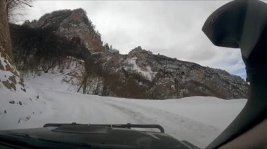 Sürücü virajlı ana yola doğru arabayla gider ve yan yan yan yoldaki dev kayalar boyunca ilerler. Kafkasya 'da araba yolculuğu ön camdan görülüyor.