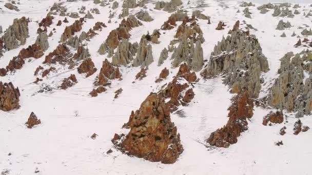 白い雪に囲まれたコーカサス山脈の裸岩のピーク 曇り空の冬の日の空中風景に急な斜面を持つ巨大な山脈 — ストック動画