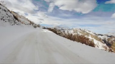 Car drives on snowy road winding in Caucasus mountains under cloudy sky. Adventurous road trip in highland on winter day view from vehicle