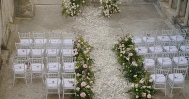 Bahçedeki süslenmiş beyaz sandalyelerin arasında taç yaprakları arasında Amalfi 'deki antik evin açık sütunlu galerisi var. Çiçekli avlu. Düğün yerinin hazırlanması