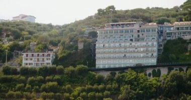 Güneşli Sorrento tepelerinde yuva yapmış turistler için modern otel binaları. İtalya 'nın güneyindeki kayalık dağlarda ağaçlarla çevrili resimli mimari
