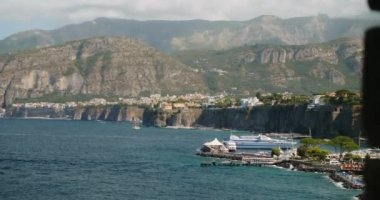 Gök mavisi deniz dalgaları Sorrento sahilindeki kayalık kayalıkları yavaşça siler. Güney İtalya 'da gün ışığıyla aydınlatılan tepelerin eteklerine saçılmış küçük kasaba evleri.