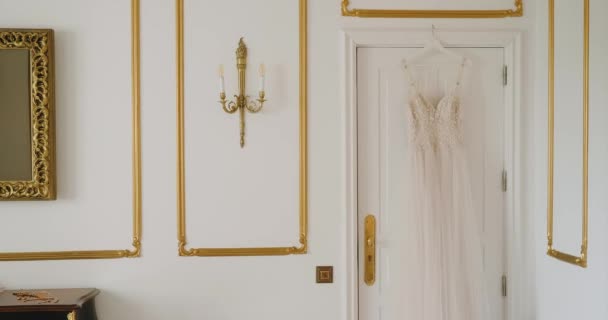 ウェディングドレスは豪華なイタリアのホテルの部屋の入り口に掛けられています 結婚式のためのさまざまな装飾が施された高価なベージュのドレス — ストック動画