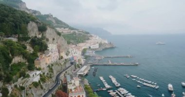 İtalya 'nın dik ormancılık dağının eteğindeki antik Amalfi kıyı kasabası. Yatları ve tekneleri olan körfez. Gökyüzünün altında bulutlarla yıkanan deniz suyu.