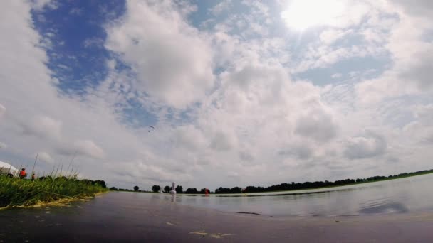 スカイダイバーは湖の近くの地面に青いパラシュートで飛ぶ スポーツマンは 積雲と青空の下で翼と呼ばれるパラシュートを使用します — ストック動画