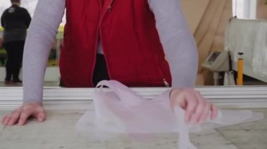 Terzi, fabrika atölyesindeki büyük kesim masasından tekstil ayrıntıları alıyor. Terzi, paraşüt imalatı için dikiş kalıpları hazırlıyor.