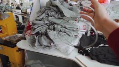 Kadın, paraşüt dikiş atölyesindeki katlanmış kumaş parçalarına karşı metal yay tutuyor. Çalışan, açılış mekanizmasının ayrıntılarını gösterir