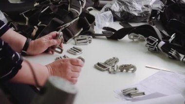 İş arkadaşı olan olgun bir kadın paraşüt ayrıntıları için metal karabinaları kontrol ediyor atölyeye yakın çekim yapıyor. İşçiler spor aletleri için donanım hazırlıyorlar