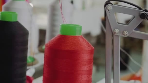 縫製工場の閉鎖中のミシンツール上の赤い糸を持つ大きなスプール オーダーメイドのアトリエでのドレッシング用品のコイル — ストック動画
