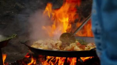 Şef, Paella malzemelerini açık ateşte kızartma tavasında karıştırıyor. Profesyonel, geleneksel İspanyol yemeği izleme sürecini akşam dikkatlice izliyor
