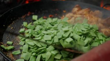 Aşçı, paella malzemelerini açık ateşte karıştırır. Duman tabağın üzerinde beliriyor, aroma ekliyor ve doğayla bağlantı hissi yaratıyor.