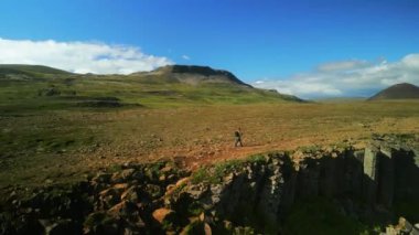 Sırt çantalı bir adam uçurum boyunca panoramik manzaranın tadını çıkararak yürüyor. Büyüleyici manzara turistleri İzlanda 'yı keşfetmeye çekiyor.