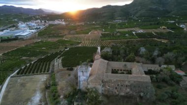 Gün doğumunda bahçelere ve tarlalara karşı kulesi olan eski bir kale. Dağ vadisindeki Sant Jeroni de Cotalba Kraliyet Manastırı